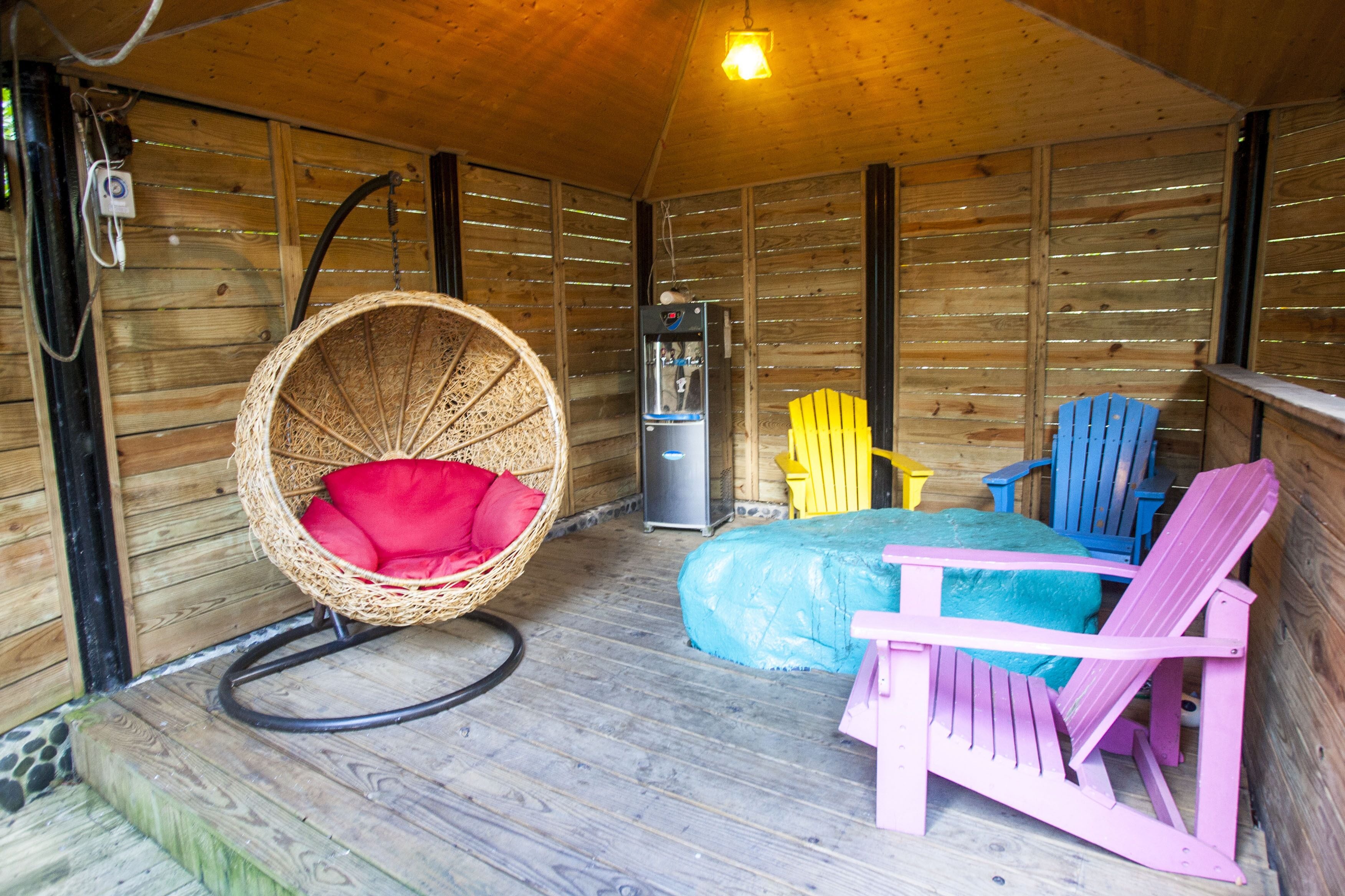 L’intérieur d’un chalet en bois, avec un fauteuil en osier, un lit et des chaises Adirondack aux couleurs vives.