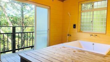 Una terraza de madera que conduce a un baño con bañera, ventana y puerta.