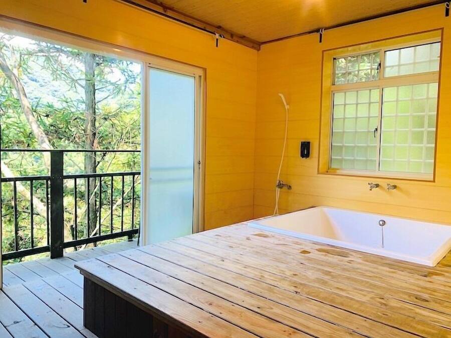 Una terraza de madera que conduce a un baño con bañera, ventana y puerta.
