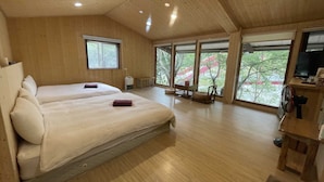 Una habitación amplia con dos camas, ventanas grandes, techo de madera y un televisor sobre un mueble de madera.
