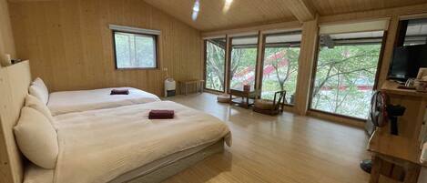 Una habitación amplia con dos camas, ventanas grandes, techo de madera y un televisor sobre un mueble de madera.