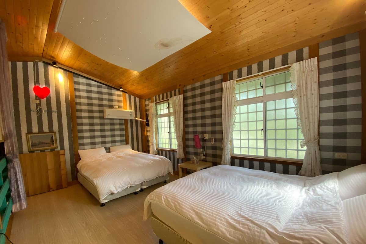 A room with two beds, checkered walls, a wooden ceiling, and a window with curtains.