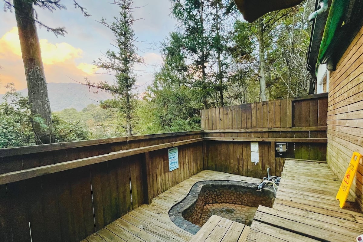 A wooden deck with a hot tub, surrounded by trees and a wooden fence.