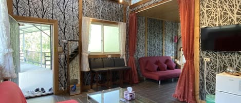 Una habitación amplia con techo alto, un ventanal grande, un sofá, una mesa y un televisor.