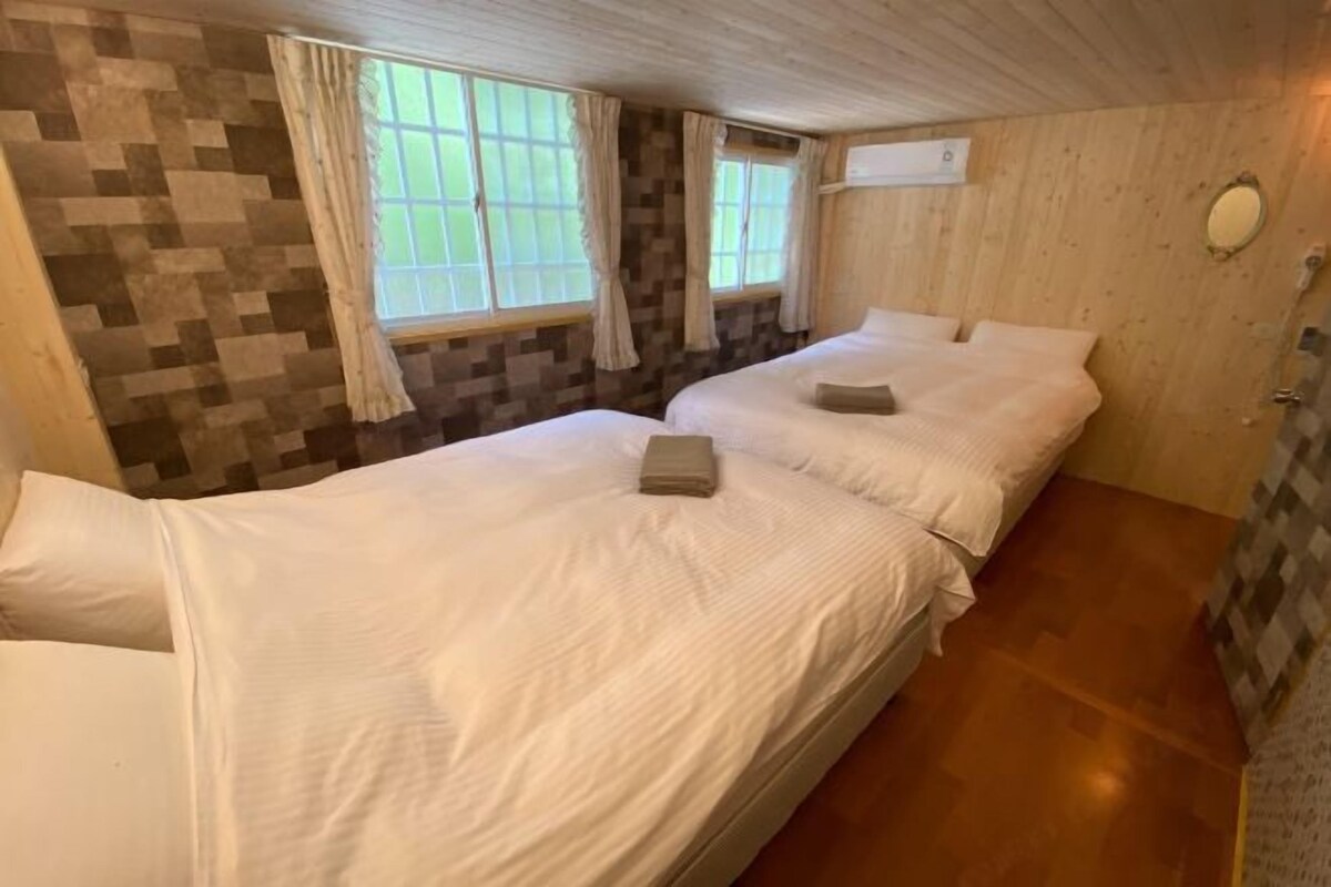 Une chambre avec deux lits, une fenêtre avec des rideaux, un mur en bois et un petit miroir.