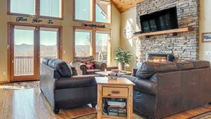 A spacious living room with a stone fireplace, leather sofas, and large windows offering a view of the mountains. - Pool, Hot Tub & Mountain Views: Cleveland Cabin (Cleveland)