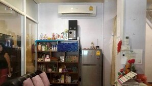 Un espacio habitable compacto con un sofá de cuero negro, una mesita de centro y una zona de cocina que incluye un refrigerador y un estante con diversos objetos.