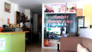 Zona de recepción con mostrador verde, sofá marrón y señalización de masajes y spa.