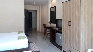 Una habitación de hotel con cama, escritorio con ordenador, armario y un refrigerador pequeño.