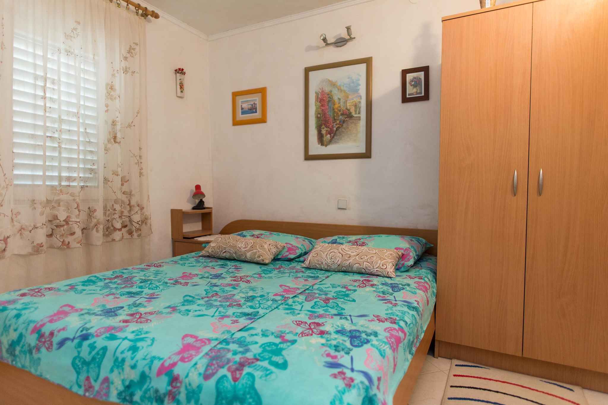 A bedroom with a bed, a wooden wardrobe, a bedside table, and a window with curtains.