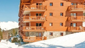 Un edificio de madera de varios pisos con balcones, frente a un paisaje montañoso nevado.
