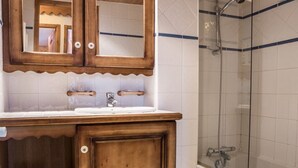 Un baño con tocador de madera, un espejo, lavamanos y cabina de ducha con puerta de vidrio.