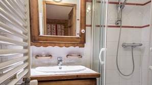 Un baño con tocador de madera, lavamanos blanco, espejo y cabina de ducha de vidrio.