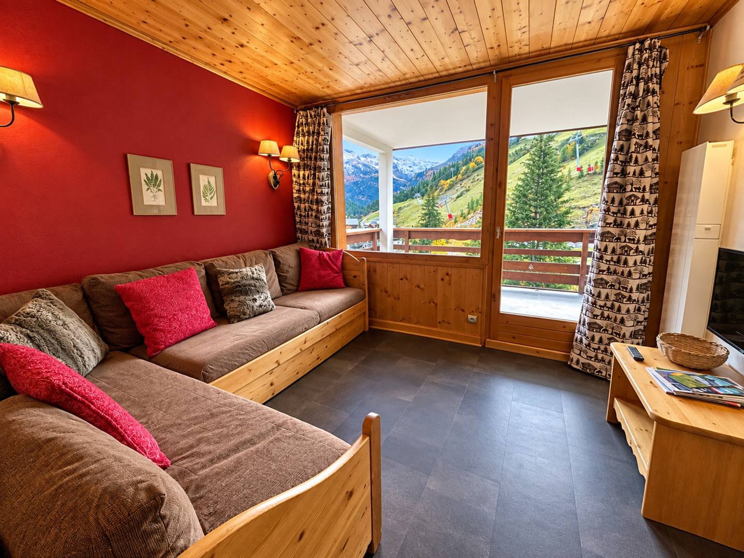 A cozy room with a wooden ceiling, a red wall, a large window with a mountain view, and a wooden bench.
