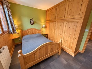 Een houten bed in een kamer met een groene wand, een decoratie van een hertenkop en een houten garderobe.