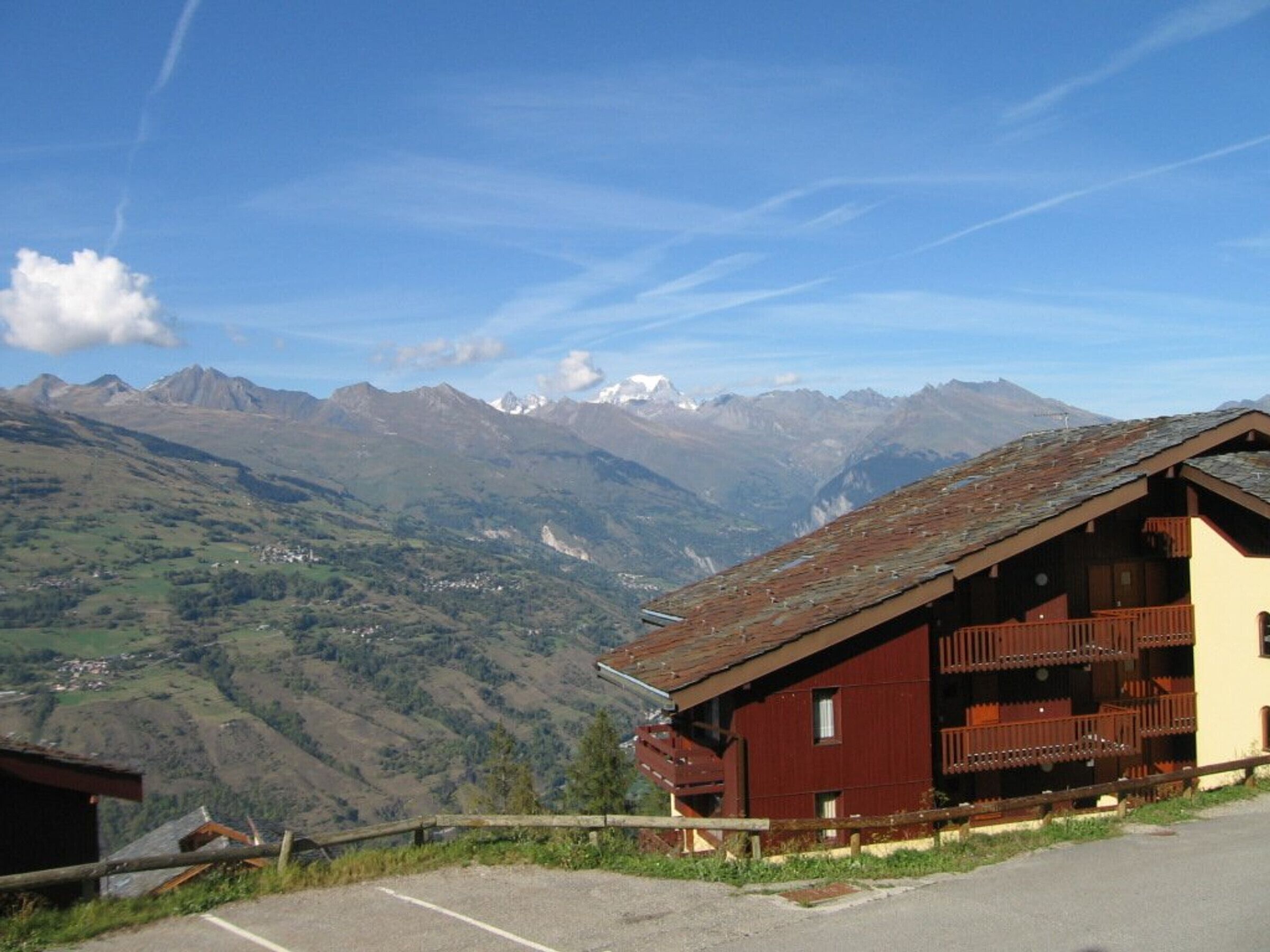 A mountain lodge with a wooden balcony, surrounded by a scenic mountain view.