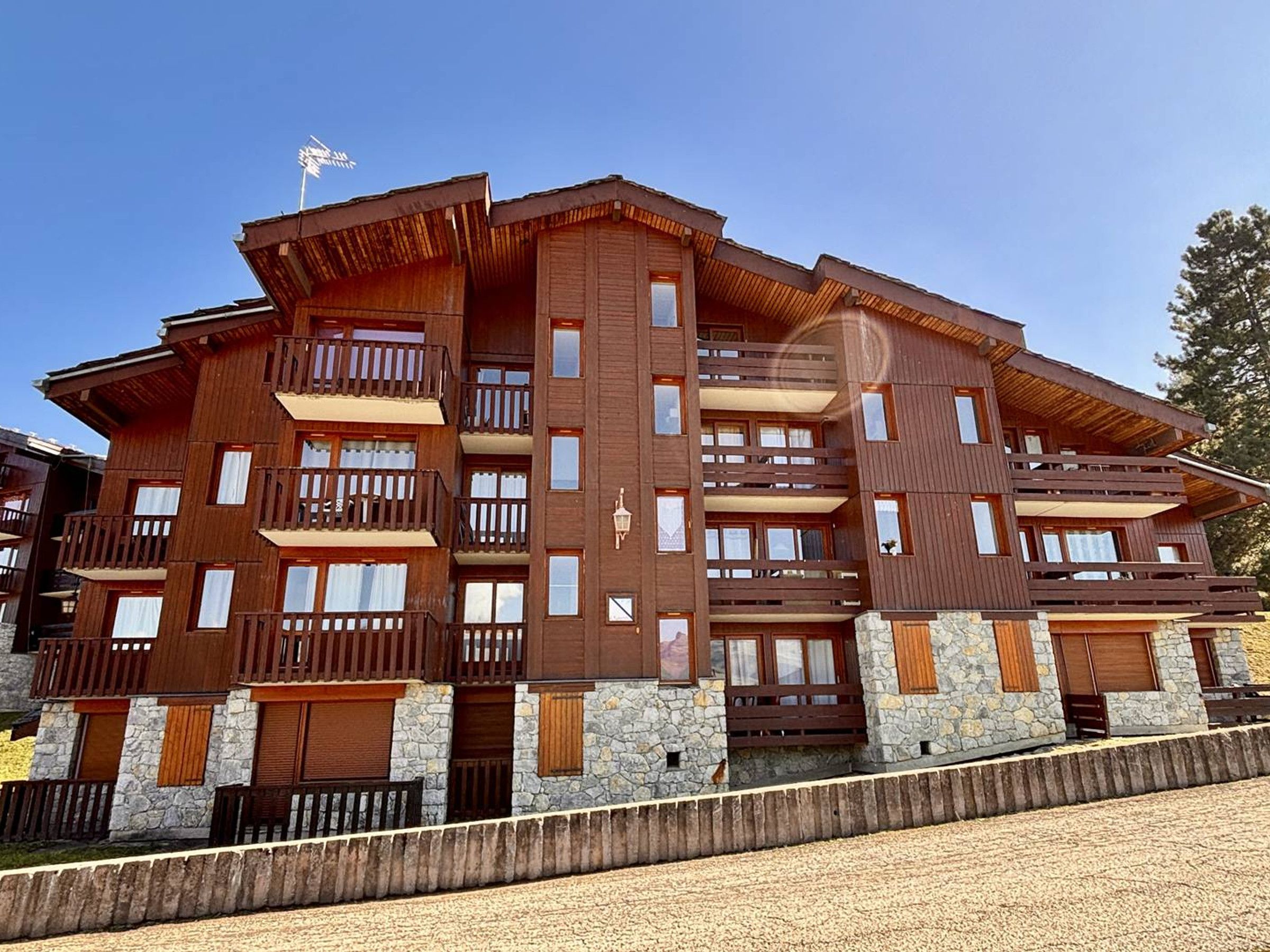 A multi-story wooden building with balconies, stone accents, and a clear sky.