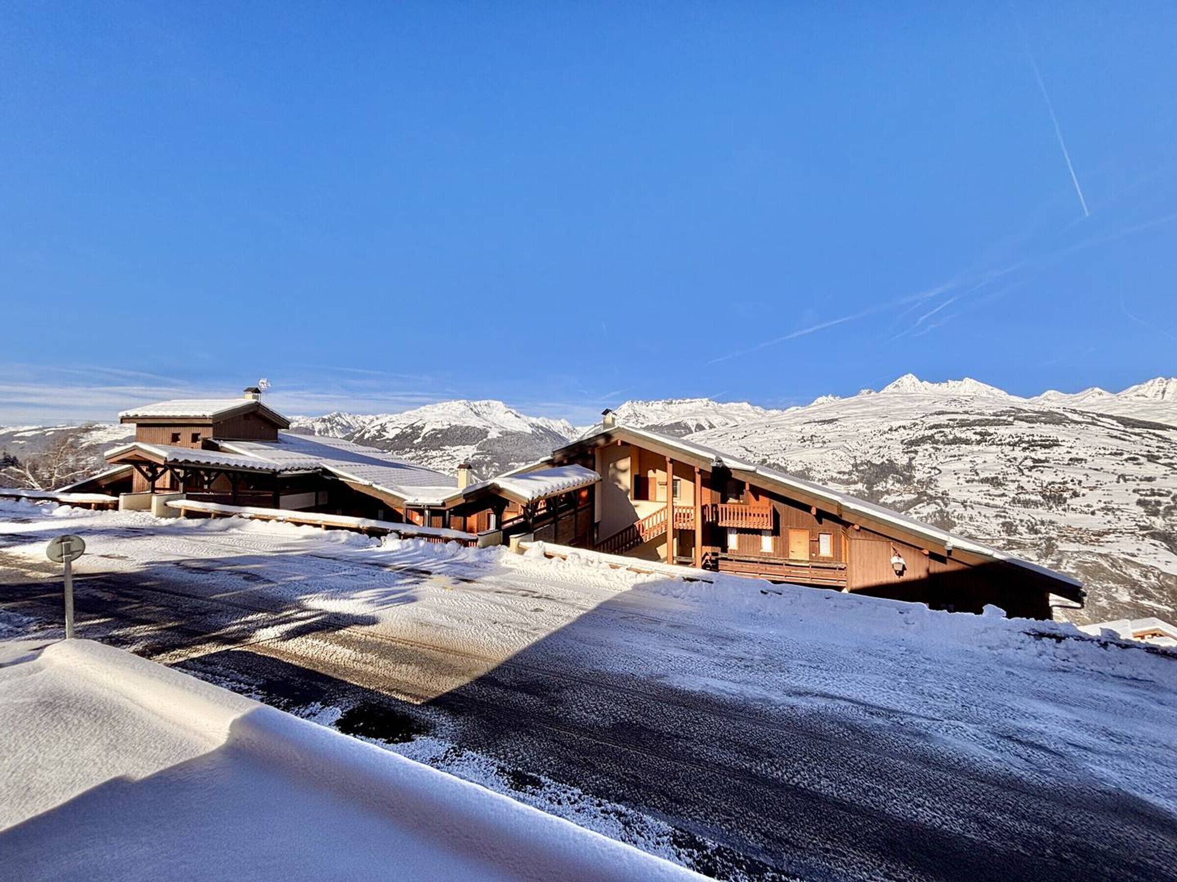 Un chalet de montagne enneigé, doté d’une architecture en bois et offrant une vue dégagée sur les montagnes aux sommets enneigés qui se dressent à l’arrière-plan.