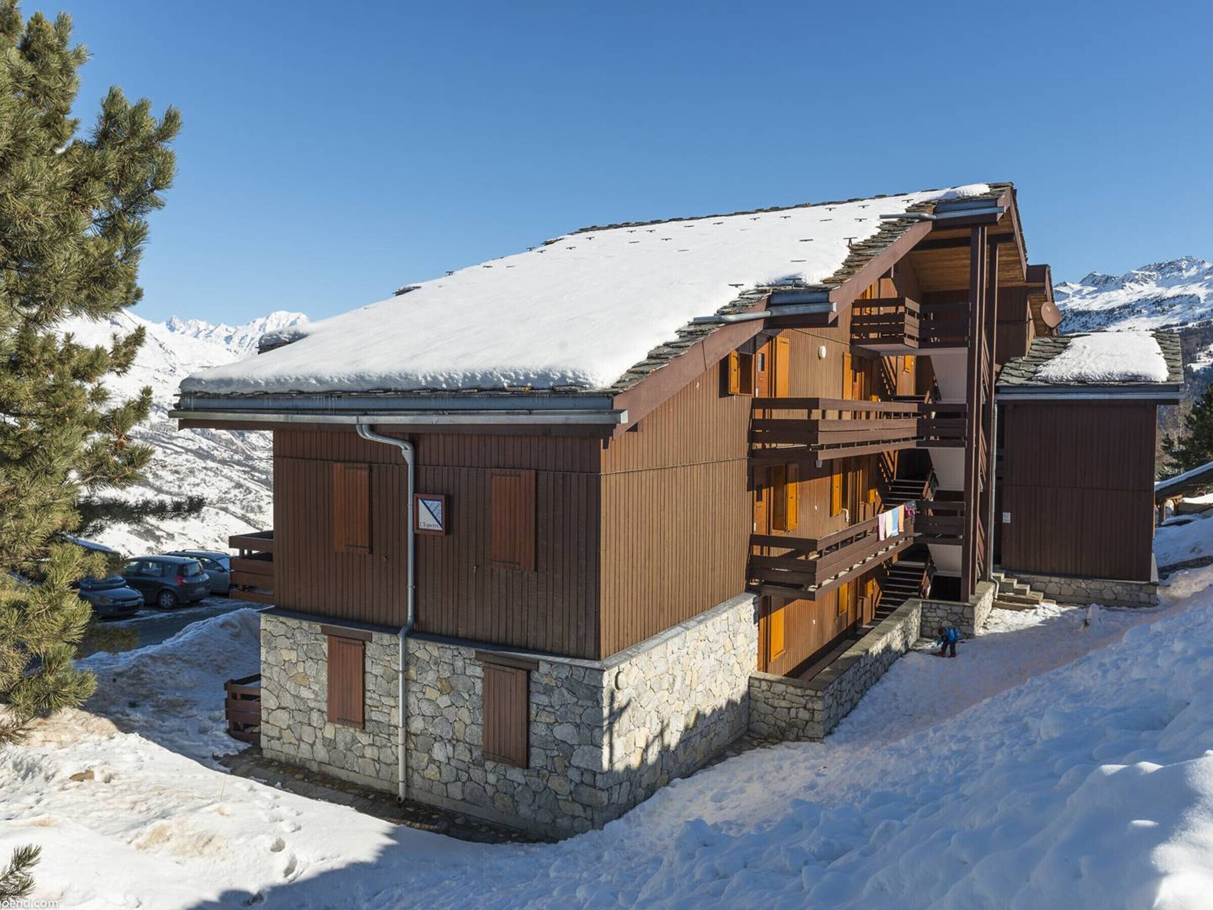 Een houten chalet met een stenen fundering, houten balkons en een trap naar een hoger gelegen niveau.