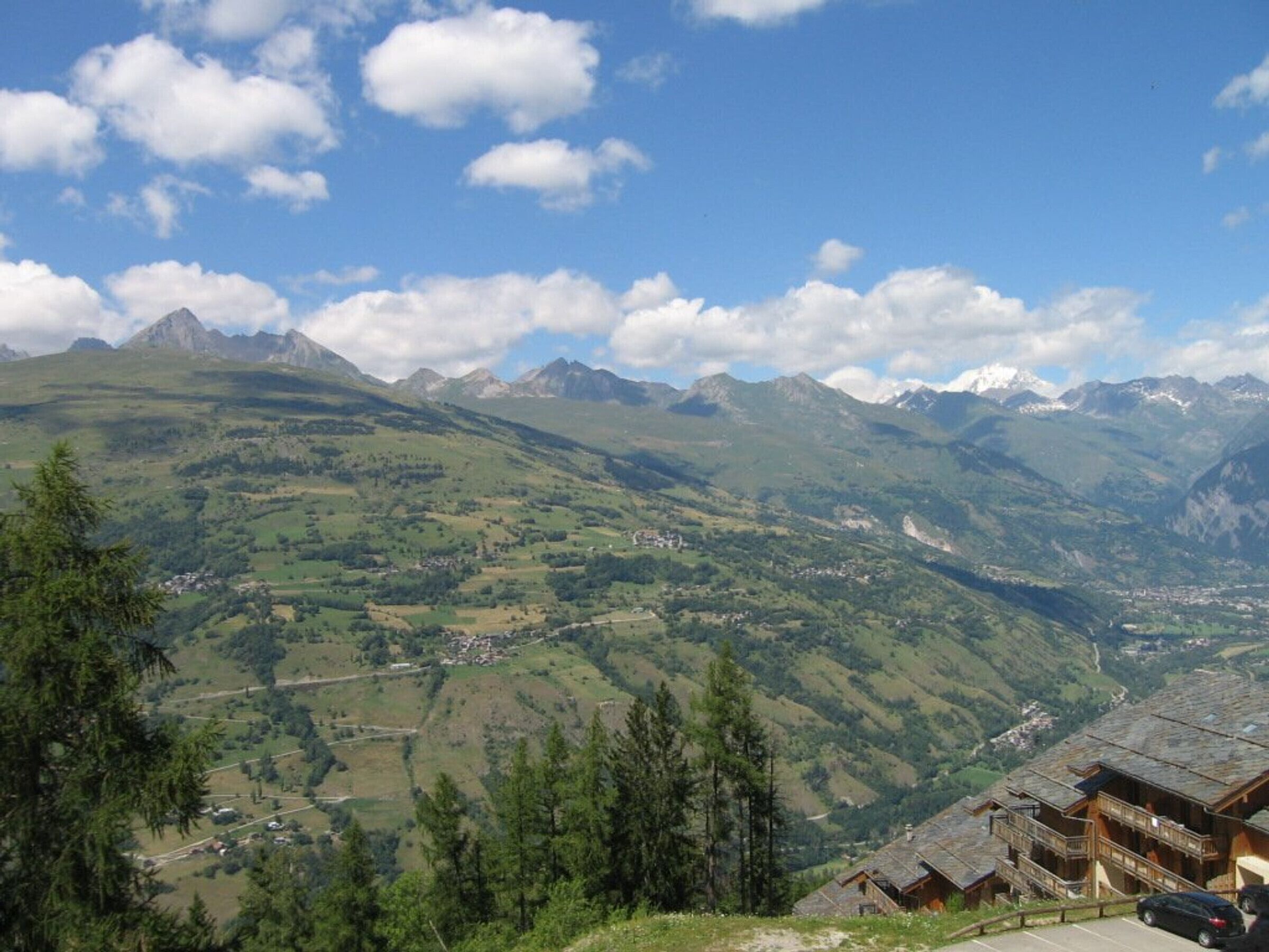 Un chalet de montagne offrant une vue sur une vallée et des sommets lointains.
