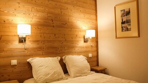 Une chambre d’hôtel avec une tête de lit en bois, deux lampes de chevet, un lit avec une literie blanche, une table de chevet et un tableau encadré au mur.