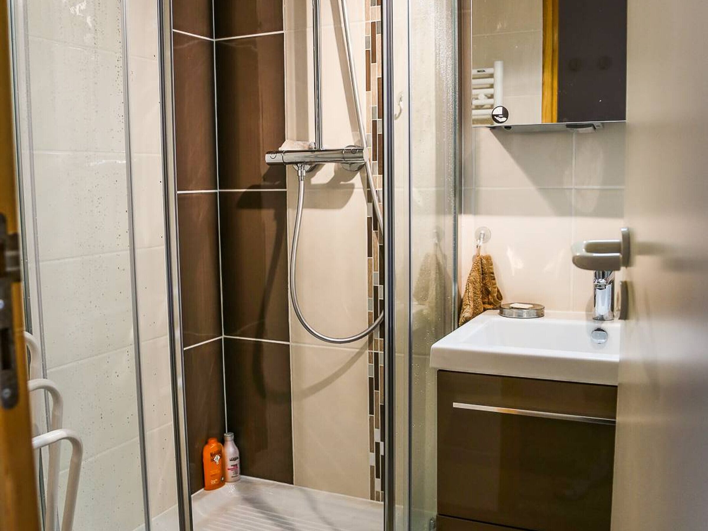 Ein modernes Badezimmer mit einer gläsernen Duschkabine, einem weißen Waschbecken und einem Spiegel darüber.