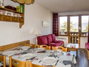 A dining area with a table set for four, wooden chairs, a red sofa, and a window with a view of trees and mountains. - 3-Room Apt, 6 ppl, near slopes, pets allowed - La Plagne (La Plagne)
