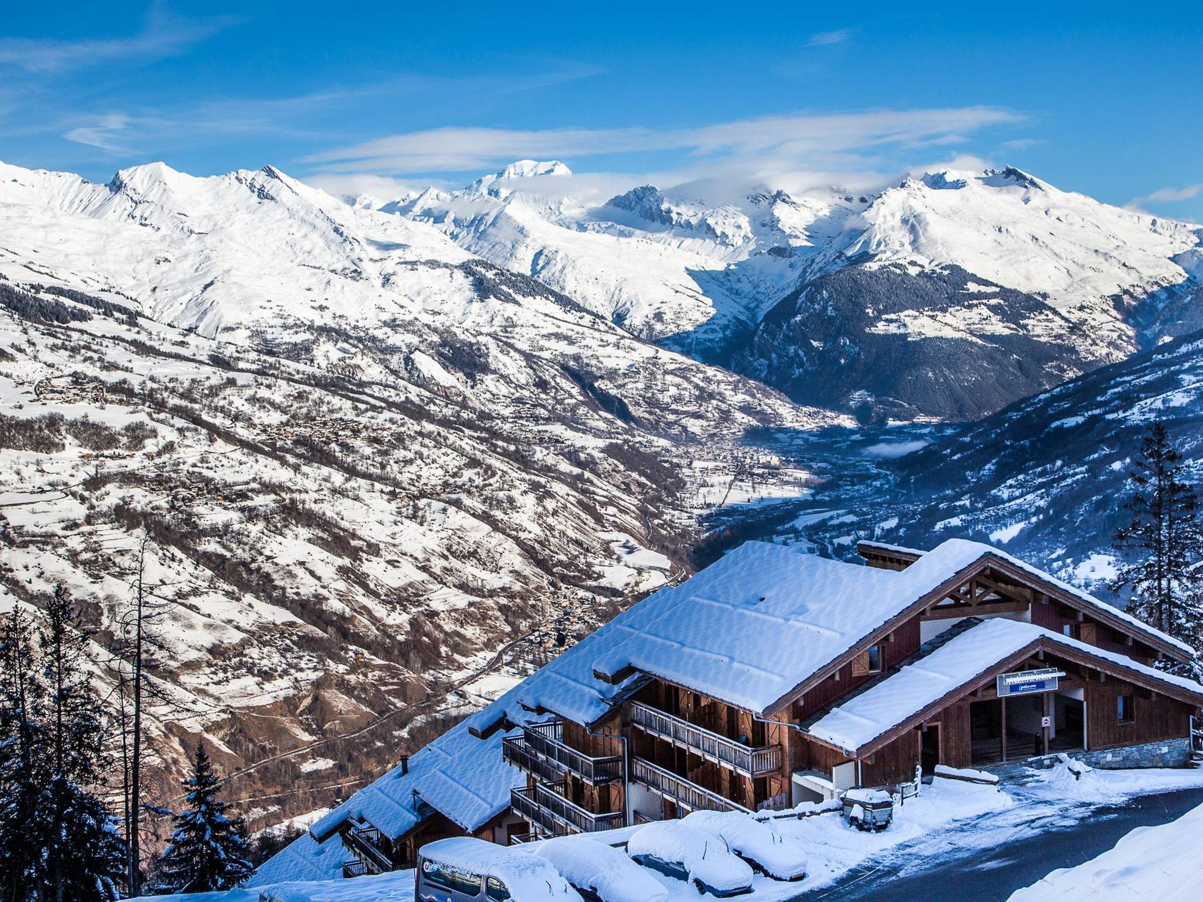 Un chalet en bois, dont le toit est recouvert de neige, situé au pied d’une chaîne de montagnes.