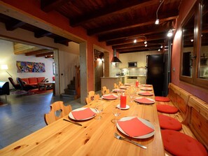A dining area with a long wooden table set for a meal, a kitchen in the background, and a staircase leading to another level. - Comfortable chalet, mountain view - 9 guests (La Plagne Tarentaise)
