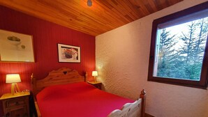 A room with a wooden bed, two bedside tables with lamps, a framed picture on the wall, and a window with a view of trees.