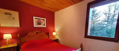Una habitación con una cama de madera, dos mesitas de noche con lámparas, un cuadro en la pared y una ventana con vista a árboles.