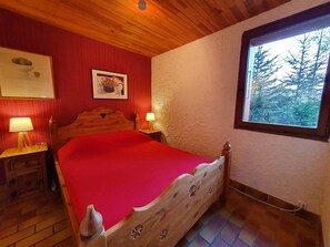 A room with a wooden bed, two bedside tables with lamps, a framed picture on the wall, and a window with a view of trees.