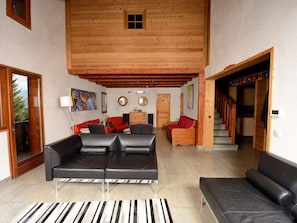 A spacious living area with a high ceiling, a wooden staircase, and a view of the outdoors.