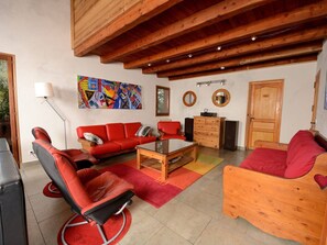 A modern living room with red furniture, a colorful abstract painting, wooden beams, and a large window. - Comfortable chalet, mountain view - 9 guests (La Plagne Tarentaise)