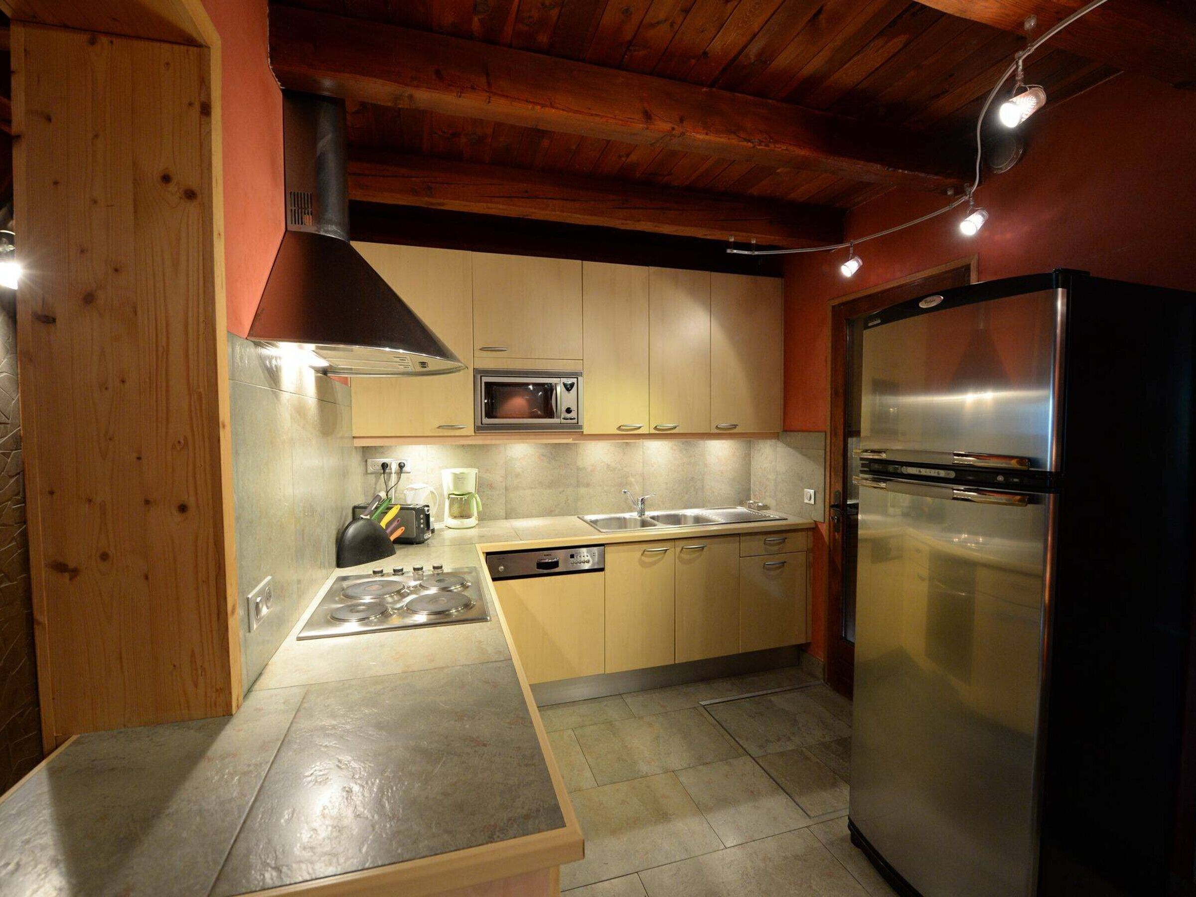 A compact kitchen with a stove, microwave, sink, and stainless steel refrigerator.
