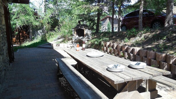 An outdoor dining area with a stone wall, wooden benches, and a stone table.