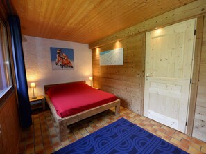 A wooden-paneled room with a bed, a painting, a wall-mounted light, and a door. - Comfortable chalet, mountain view - 9 guests (La Plagne Tarentaise)