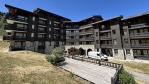 A multi-story hotel with balconies, stone facade, and a wooden deck. - Charming 2-room flat with terrace and new kitchen in the heart of Méribel, direct access to slopes (Les Allues-Méribel)
