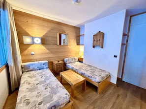 Una habitación acogedora con dos camas individuales, una mesita de madera, un espejo y un armario empotrado.