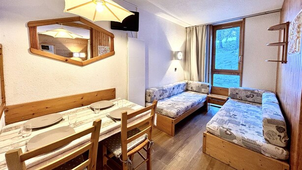 A cozy room with a wooden dining table, chairs, a sofa, and a large window with curtains.