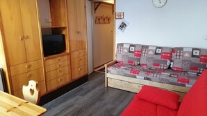 A compact living space with a wooden wardrobe, a television, a sofa with a patchwork cover, and a clock on the wall. - Cozy studio in Plagne Villages near slopes, balcony, 4 ppl (La Plagne)