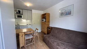 Un espace de vie compact comprenant un coin cuisine, une table à manger avec des chaises et un canapé marron.