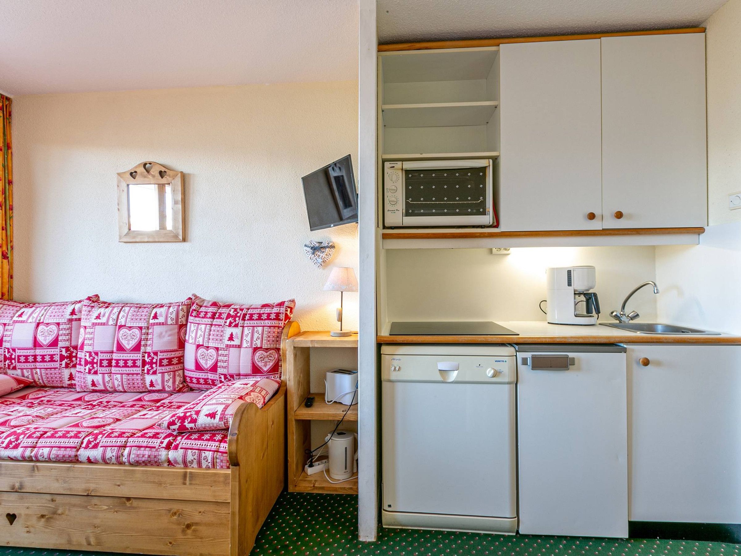 A compact room with a wooden bed, a kitchenette with a microwave, a coffee maker, and a sink.