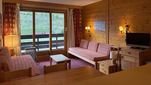 A cozy room with a wooden interior, a sofa, a table, a television, and a window with curtains.