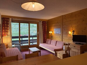 A cozy room with a wooden interior, a sofa, a table, a television, and a window with curtains.