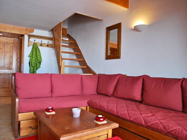 Un salon chaleureux avec un escalier en bois, un canapé rouge et une petite table en bois sur laquelle sont posées deux bougies rouges.