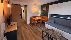 A compact living space with a wooden floor, a sofa, a dining table with chairs, and a small TV on a stand. - Cozy studio for 2, terrace, pets allowed (La Plagne)