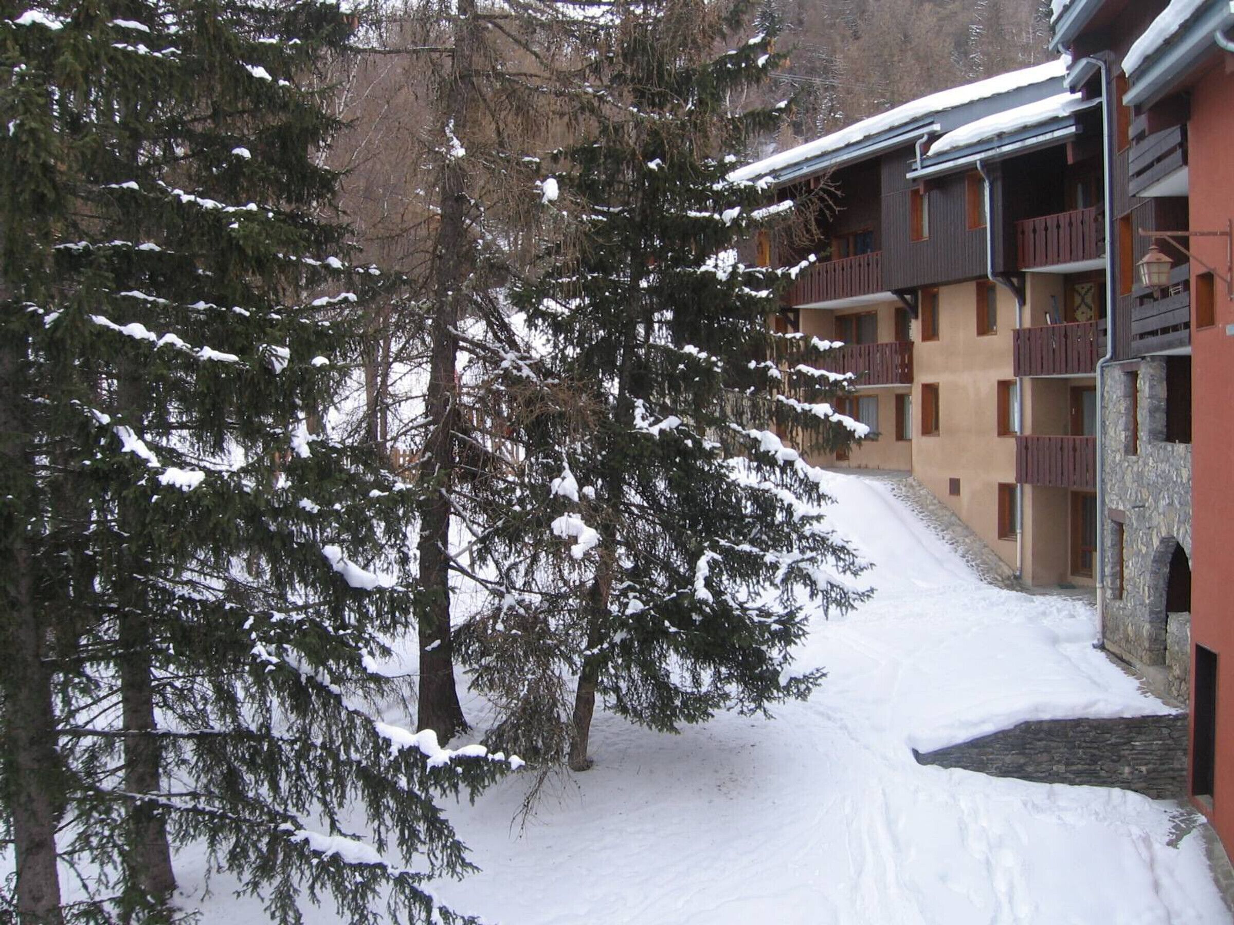 Ein verschneiter Innenhof mit einem Gebäude, das Balkone und eine Steinmauer aufweist.
