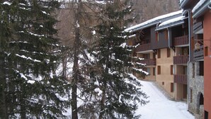 Un patio cubierto de nieve con un edificio que cuenta con balcones y un muro de piedra.