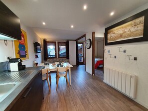 A compact kitchen with a dining area, wooden flooring, and a view through the windows.